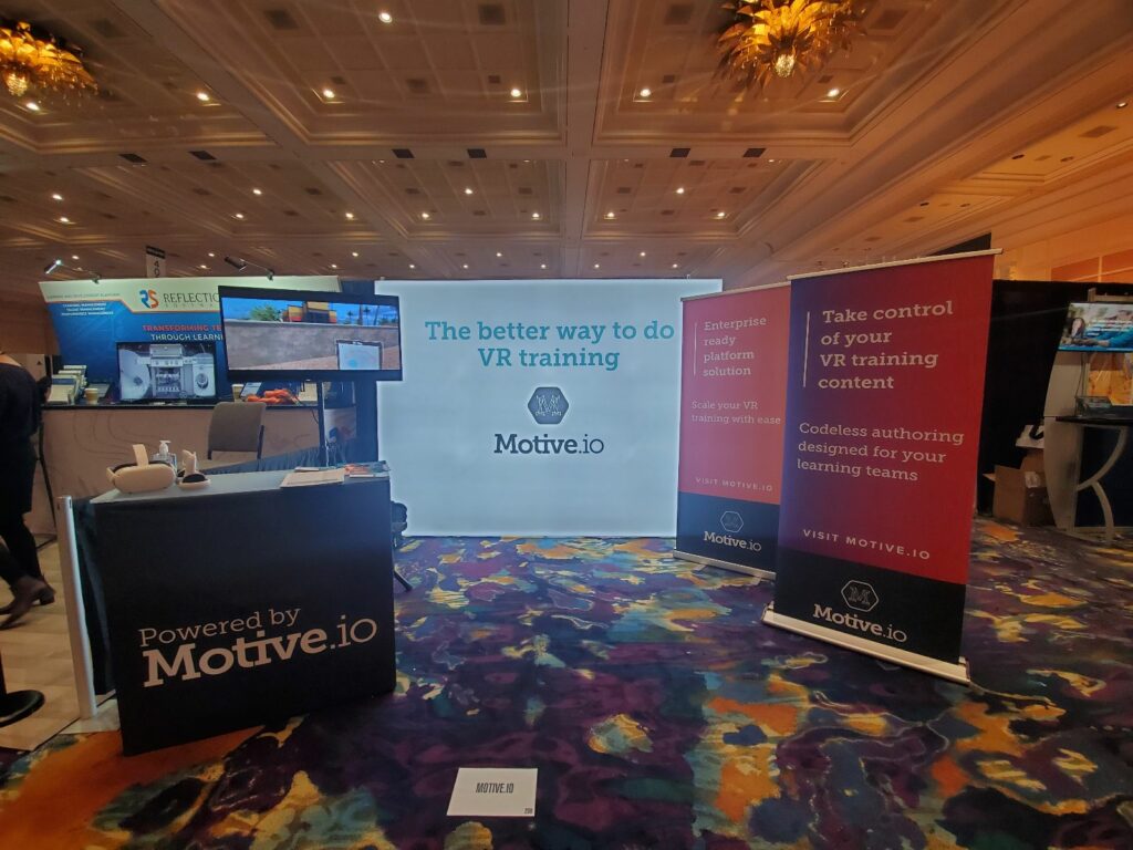 DevLearn set up for Motive.io including banners, backdrop, podium, and TV.